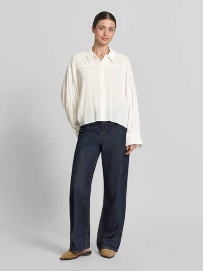 Frauenmodel trägt Relaxed Fit Bluse Modell 'SELENI' von Drykorn aus Baumwoll-Viskose-Mix mit Hemdblusenkragen und Knopfleiste, Ganzkörperansicht von vorne. Rückenlänge bei Größe 36: 59 cm, Ärmellänge: 63 cm.