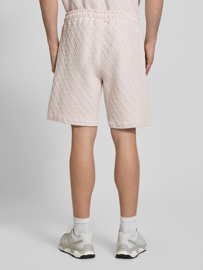 Mężczyzna nosi szorty Relaxed Fit Sweatshorts mit Strukturmuster model 'Jovren' od Pegador, elastyczna mieszanka materiałów z mieszanką bawełny, kolor jasnoróżowy, fakturowany wzór, szerokość w rozmiarze M: 39 cm, długość wewnętrzna nogawki: 24 cm, widok całej sylwetki od tyłu.