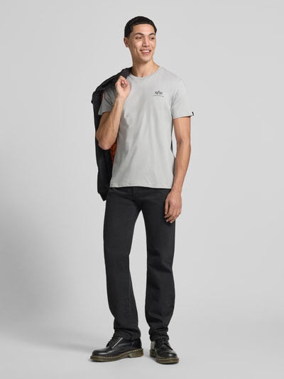 Männermodel trägt T-Shirt mit Label-Details Modell 'BASIC' von Alpha Industries in Grau, Gerader-Schnitt, Reine Baumwolle, Ganzkörperansicht von vorne.