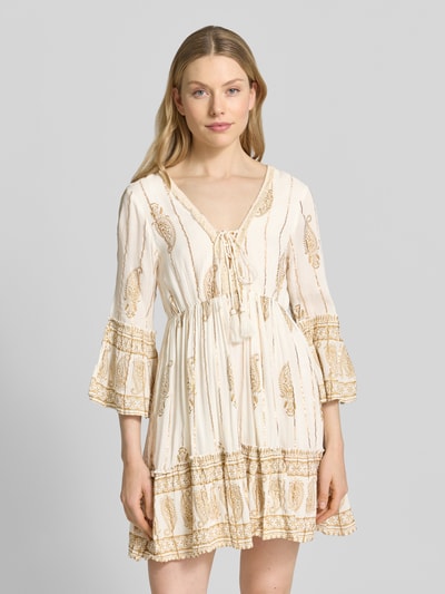 Frauenmodel trägt Minikleid mit Allover-Paisley-Print von Apricot aus Viskose-Mix, Taillierte Passform, V-Ausschnitt, 3/4-Arm, Schnürverschluss, Rüschenbesatz, in Creme und Beige-Tönen, Stoff mit leichter Struktur, Nahaufnahme Oberkörper.