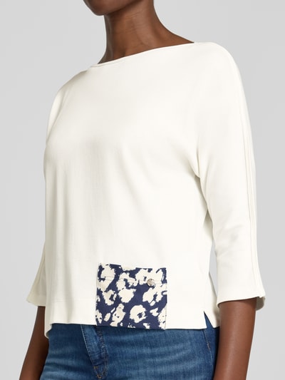 Frauenmodel trägt Regular Fit T-Shirt mit Logo-Detail von Marc Cain in Weiß mit blauem Print, elastischer Baumwoll-Mix, U-Boot-Ausschnitt, 3/4-Arm, Rückenlänge 49 cm, Nahaufnahme Oberkörper.