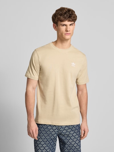 Männermodel trägt T-Shirt mit Label-Stitching von adidas Originals in Beige, reine Baumwolle, Regular Fit, Nahaufnahme Oberkörper.