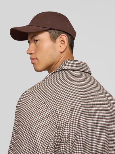 Männermodel trägt Trenchcoat mit Knopfleiste und Label-Patch von ANOTHER COTTON LAB in braun kariertem Muster, Nahaufnahme Rückansicht. Gerader Schnitt, Kentkragen, strukturierte Gewebeoberfläche.