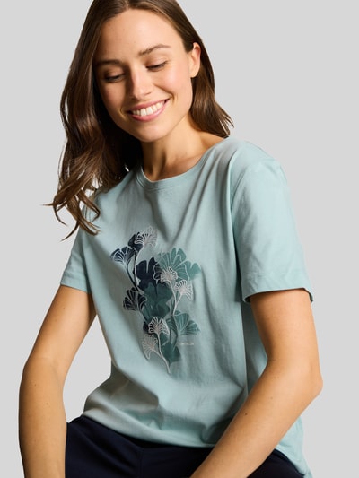 Frauenmodel trägt Regular Fit T-Shirt aus reiner Baumwolle von Tom Tailor, Optik: Unifarben, Motiv-Print-Stitching, Label-Print, Rundhals, Kurzarm, Rumpfabschluss mit Seitenschlitzen, Materialverarbeitung: Jersey, Ganzkörperansicht von vorne.
