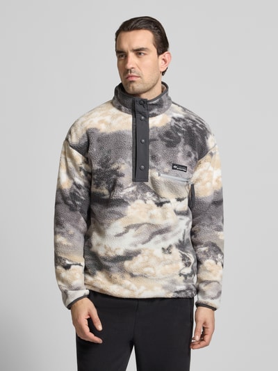 Männermodel trägt Regular Fit Pullover mit Logo-Patch von Columbia w efekt marmurkowy, kieszeń na piersi z zamkiem, stójka z listwą z zatrzaskami, elastyczne wykończenia, długość tyłu 72 cm, długość rękawów 49 cm, cała sylwetka z przodu