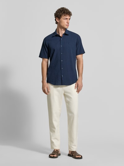Männermodel trägt Relaxed Fit Freizeithemd mit Logo-Stitching und Kentkragen von Lerros aus dunkelblauem Seersucker, Knopfleiste, abgerundeter Saum, Rückenlänge Größe M 75 cm, Schulterbreite 45 cm, Ärmellänge 25 cm, Ganzkörperansicht von vorne.