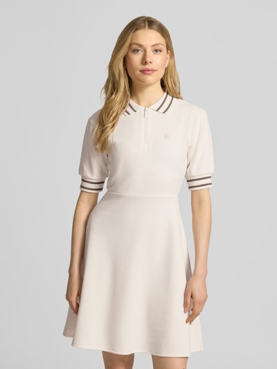 Vrouwenmodel draagt Minikleid met Polokragen en Logo-Stitching van ARMANI EXCHANGE in licht beige, materiaalmix met viscose, getailleerd model, polokraag, korte ritssluiting, gestikt logo, ruglengte maat S 92 cm, borstwijdte 47 cm, mouwlengte 28 cm, frontale bovenlichaam close-up.