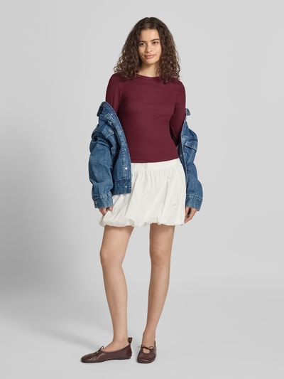Frauenmodel trägt Slim Fit Langarmshirt aus Baumwoll-Mix Modell 'VAL' von ONLY, weinrot, mit Jeansjacke und weißem Rock, Ganzkörperansicht von vorne. Damen Langarmshirt von ONLY.