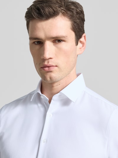 Męski model nosi Slim Fit Business-Hemd in kurzärmligem Design Modell 'Modern' von OLYMP Level Five, biały kolor, mieszanka bawełny z domieszką stretchu, krój slim fit, kołnierz kent, zapięcie na guziki, krótki rękaw, długość pleców w rozmiarze 40: 79 cm, szerokość w rozmiarze 40: 43 cm, długość rękawa w rozmiarze 40: 24 cm, zbliżenie na górną część ciała