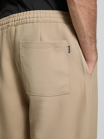 Männermodel trägt Straight Fit Stoffhose mit Viskose-Anteil von REVIEW in Beige, sichtbare Gesäßtasche, elastischer Bund, Nahaufnahme Hüfte.