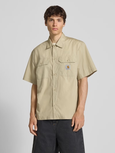 Männermodel trägt Relaxed Fit Freizeithemd mit Kentkragen und Label-Detail von Carhartt Work In Progress im Material-Mix, beige, mit Brusttaschen; Rückenlänge 75 cm, Schulterbreite 51 cm, Ärmellänge 28 cm, Ganzkörperansicht von vorne.
