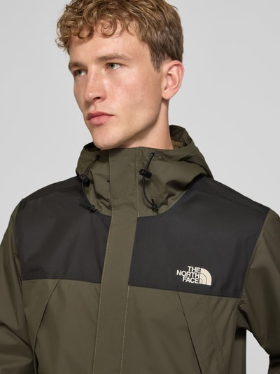 Männermodel trägt Jacke mit Label-Print Modell 'ANTORA' von The North Face in Oliv und Schwarz, Reißverschlusstaschen, Nahaufnahme Oberkörper.