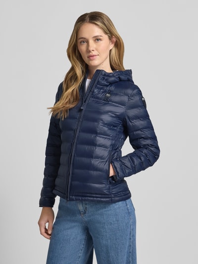 Frauenmodel trägt Steppjacke mit Zweiwege-Reißverschluss Modell 'ELLIS' von Blauer Usa in Dunkelblau, glänzende Textur, Kapuze, Ganzkörperansicht von vorne. Slim Fit, sichtbare Nähte, passende Jeans, Rückenlänge 57 cm, Schulterbreite 35 cm, Brustweite 48 cm, Ärmellänge 60 cm.
