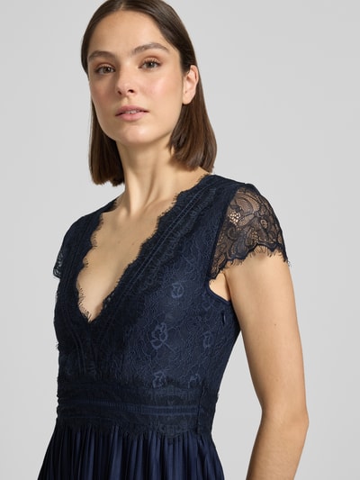 Frauenmodel trägt Abendkleid in Falten-Optik Modell 'Emelie' von GUIDO MARIA KRETSCHMER WOMAN aus dunkelblauem Satin mit Spitzenbesatz, taillierter Passform und V-Ausschnitt, Nahaufnahme Oberkörper.