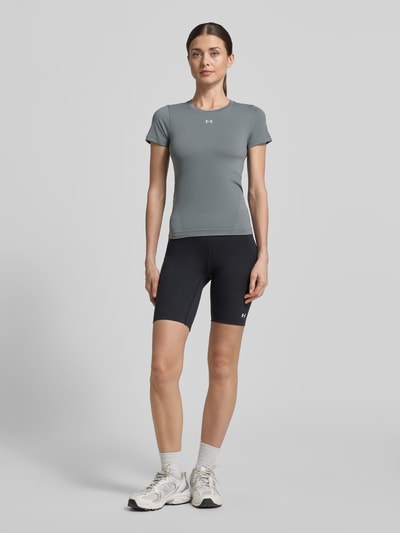 Vrouwenmodel draagt T-shirt met ronde hals en logo van Under Armour, slim fit, materiaalmix met stretch, ruglengte maat S 54 cm, volledig lichaamsaanzicht van voren.