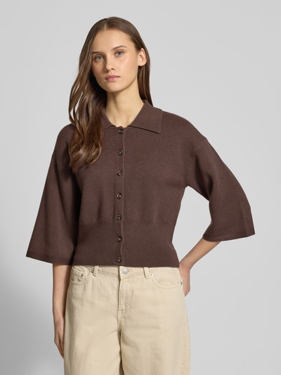 Frauenmodel trägt Strickjacke aus Viskose-Mix Modell 'SHYLA' von Noisy May in Braun mit Umlegekragen, durchgehender Knopfleiste, 3/4-Arm und gerippten Abschlüssen, lockere Passform, Rückenlänge 48 cm, Nahaufnahme Oberkörper.