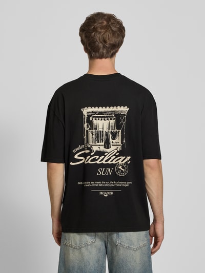 Männermodel trägt Oversized T-Shirt mit rückseitigem Print Modell 'Pedroche' von Pegador in Schwarz, Motiv in Beige, Puur katoen, oversized fit, Ganzkörperansicht Rückansicht.