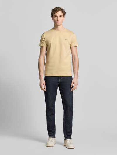 Männermodel trägt T-Shirt mit Label-Detail von Gant in Beige, reine Baumwolle, gerader Schnitt, Rundhalsausschnitt, Ganzkörperansicht von vorne.