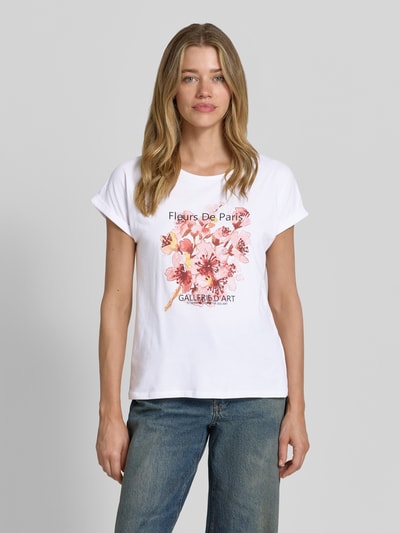 Frauenmodel trägt Damen T-Shirt mit Motiv-Print Modell 'RINA' von Soyaconcept, Weiß mit floralem Print, Baumwoll-Elasthan-Mix, Regular-Fit, Rundhalsausschnitt, Ärmel mit Aufschlag, Rückenlänge 61 cm in Größe S, Ganzkörperansicht von vorne.