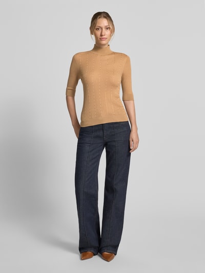 Frauenmodel trägt Slim Fit Longsleeve aus reiner Lanawolle Modell 'Maglia Costine' von Liu Jo White, beige, semitransparent, 1/2-Arm, Stehkragen, feine Rippenstruktur, kombiniert mit dunkler Jeans, Ganzkörperansicht von vorne.