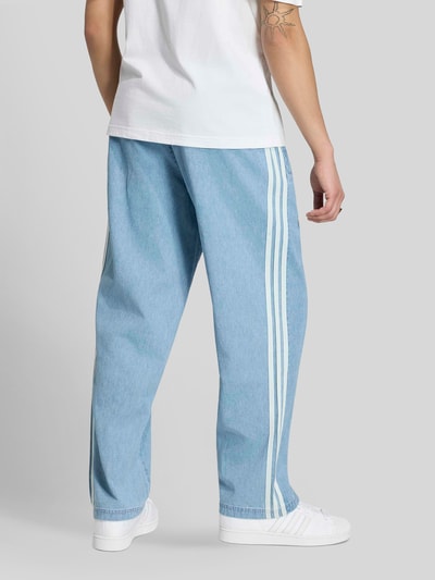 Männermodel trägt Relaxed Fit Trainingshose aus Baumwoll-Mix von adidas Originals in Denim-Optik mit Logo-Applikation, Ganzkörperansicht Rückansicht.