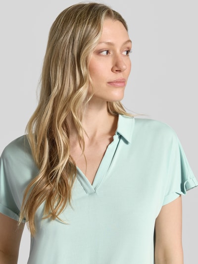 Frauenmodel trägt Regular Fit Poloshirt aus Modal-Mix von Christian Berg Woman in hellem Mint mit V-Ausschnitt und Aufschlag an den Ärmeln, Nahaufnahme Oberkörper. Damen Poloshirt, Rückenlänge bei Größe S: 46 cm.