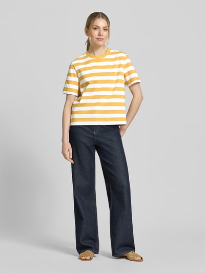 Frauenmodel trägt Boxy Fit T-Shirt aus reiner Baumwolle Modell 'ESSENTIAL' von Selected Femme, Optik:Allover-Muster, gestreift, Label-Patch, Rundhals, Ärmelform: Kurzarm, Materialverarbeitung: Jersey, Farbe Gelb und Weiß, Ganzkörperansicht von vorne.