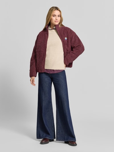 Frauenmodel trägt Regular Fit Jacke aus Teddyfell Modell 'Hoktown' von American Vintage in Dunkelbeere, strukturierte Oberfläche, Ganzkörperansicht von vorne. Rückenlänge 63 cm, Schulterbreite 52 cm, Brustweite 51 cm, Ärmellänge 54 cm.