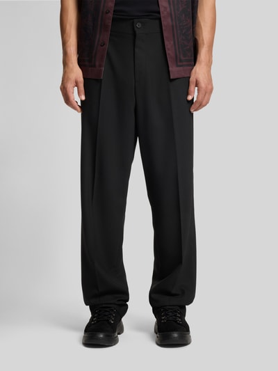 Männermodel trägt Regular Fit Anzughose mit Bügelfalten Modell 'FLIPS251X' von HUGO aus schwarzem Stretch-Twill, Nahaufnahme Oberkörper bis Schuhe.
