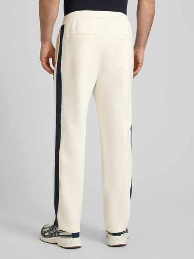 Männermodel trägt Sweatpants mit Label-Patch und elastischem Bund von ARMANI EXCHANGE aus Baumwoll-Mix mit Stretch-Anteil, Relaxed-Fit, Längsnähten, in Creme mit dunklen Seitenstreifen, Innenbeinlänge bei Größe M: 42 cm, Ganzkörperansicht Rückansicht.