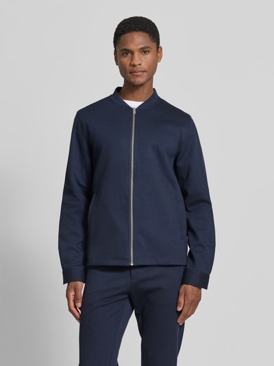 Męski model ma na sobie Regular Fit Sweatjacke mit Stehkragen od Lindbergh, elastyczna mieszanka materiałów, krój regular fit, stójka, zamek błyskawiczny, wpuszczane kieszenie, długość tyłu w rozmiarze M: 69 cm, długość rękawów w rozmiarze M: 66 cm, kolor granatowy, gładka tekstura, całkowity widok z przodu.