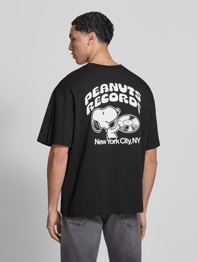 Männermodel trägt Regular Fit T-Shirt aus reiner Baumwolle Modell 'PEANUTS' von Only & Sons, schwarz mit weißem Peanuts® Print, Ganzkörperansicht Rückansicht.