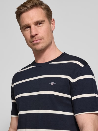 Męski model nosi Regular Fit T-Shirt mit Logo-Stitching von Gant z bawełny, okrągły dekolt, długość tyłu 68 cm w rozmiarze M, zbliżenie na górę ciała.