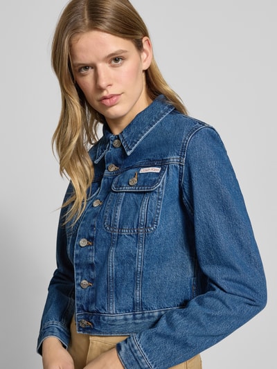Kobiece model prezentuje Kurtka jeansowa o krótkim kroju z dettagiem z logo, bawełna, wykładany kołnierz, kieszenie na piersi, listwa guzikowa, Cropped Jeansjacke mit Label-Detail od Calvin Klein Jeans, kolor niebieski, faktura denim, szerokość ramion 40 cm, długość rękawów 61 cm, szerokość klatki piersiowej 44 cm, długość tyłu 44 cm, Ganzkörperansicht z przodu.