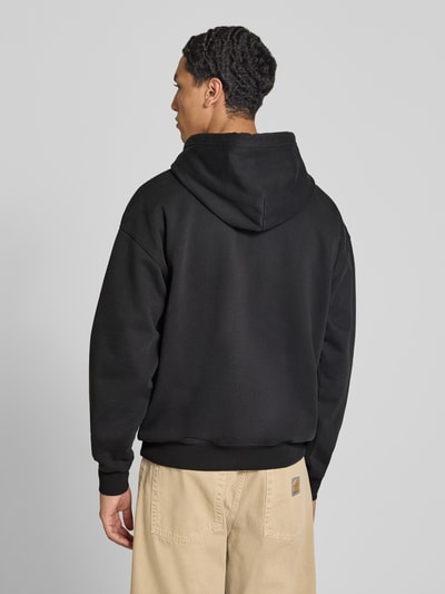 Männermodel trägt schwarzen Relaxed Fit Hoodie aus Baumwoll-Mix Modell 'JET BL' von Levi's®, beige Hose, Ganzkörperansicht Rückansicht.