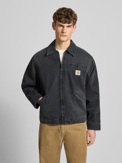 Männermodel trägt Jeansjacke mit Reißverschluss und Label-Detail Modell 'DETROIT' von Carhartt Work In Progress in Schwarz, Relaxed Fit, Baumwolle, Umlegekragen, Eingrifftaschen, Ganzkörperansicht von vorne.