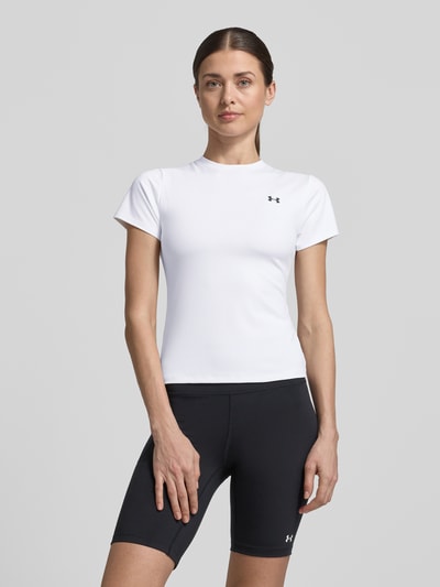 Modelka kobieca nosi T-Shirt mit Rundhalsausschnitt und Logo od Under Armour, biały, krój slim fit, materiał z domieszką stretchu, logo, długość pleców w rozmiarze S: 49 cm, pełny widok sylwetki z przodu.