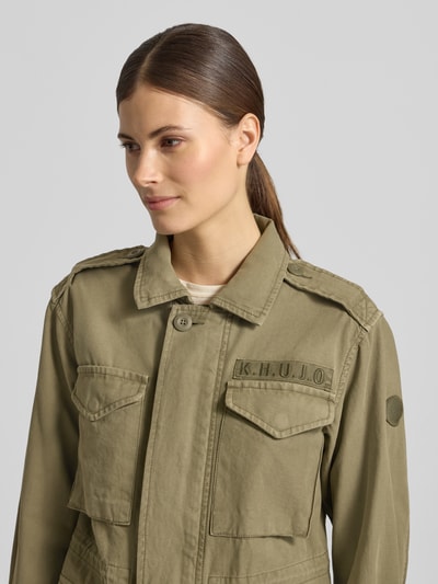 Kobiece model nosi Regular Fit kurtkę z wykładanym kołnierzem model 'Buni' od khujo, czysta bawełna, wyhaftowane logo, nakładane kieszenie, kolor khaki, szerokość ramion w rozmiarze S 40 cm, szerokość klatki piersiowej w rozmiarze S 50 cm, długość rękawów w rozmiarze S 56 cm, długość tyłu w rozmiarze S 60 cm, ujęcie: zbliżenie na górę ciała z przodu