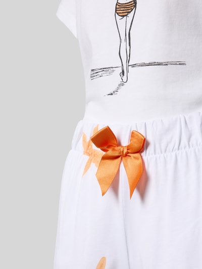 Frauenmodel trägt Pyjama-Set bestehend aus T-Shirt und Shorts Modell 'Sommerliebe' von LOUIS & LOUISA aus reiner Baumwolle mit Print-Motiv in Weiß und Orange, Regular-Fit, Detailaufnahme Shortsbereich.
