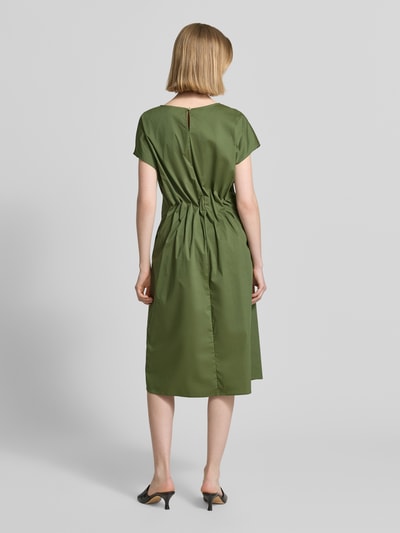 Frauenmodel trägt Midikleid mit Rundhalsausschnitt und Drapierungen von Christian Berg Woman Selection aus Baumwoll-Mix mit Stretch-Anteil, Taillierter Schnitt, Rückenlänge 108 cm bei Größe 36, Brustweite 42 cm, Farbton Olivgrün, glatte Textur, Ganzkörperansicht Rückansicht.