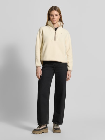 Kobiece modelka nosi Regular Fit Sweatshirt mit Stehkragen od PEAK PERFORMANCE, krój regular fit, stójka, zamek błyskawiczny, wyhaftowane logo, długość tyłu w rozmiarze S: 66 cm, szerokość ramion w rozmiarze S: 45 cm, szerokość klatki piersiowej w rozmiarze S: 57 cm, długość rękawów w rozmiarze S: 60 cm, jasny kremowy kolor, proste kształty, gładka tekstura, całkowity widok z przodu.