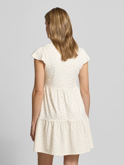 Frauenmodel trägt Minikleid im Stufen-Look mit V-Ausschnitt von REVIEW, cremefarben mit kleinen blauen Mustern, Rückenansicht, Ganzkörperansicht Rückansicht. Baumwoll-Elasthan-Mix, A-Linie, 84 cm Rückenlänge in Größe S.