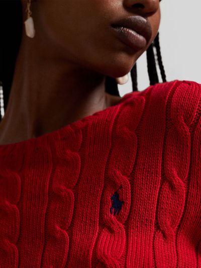 Frauenmodel trägt Strickpullover mit Zopfmuster Modell 'JULIANNA' von Polo Ralph Lauren aus roter Baumwolle, Nahaufnahme Oberkörper.