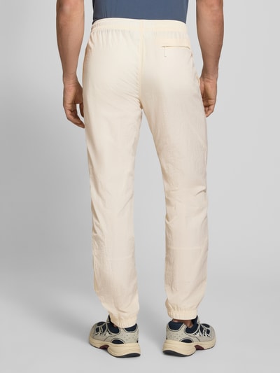 Männermodel trägt Straight Fit Stoffhose mit Logo-Stitching Modell 'Nayla' von SERGIO TACCHINI in Beige, elastischer Bund mit Tunnelzug, elastische Beinabschlüsse, Innenbeinlänge bei Größe M 77 cm, Ganzkörperansicht Rückansicht.