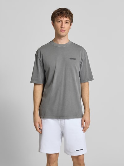 Männermodel trägt Oversized T-Shirt aus Baumwolle Modell 'Hattem' von Pegador in Grau, Oversized-Fit, Rundhalsausschnitt, Label-Detail, Ganzkörperansicht von vorne. Herren T-Shirt aus Reine Baumwolle, Rückenlänge bei Größe M: 70 cm.