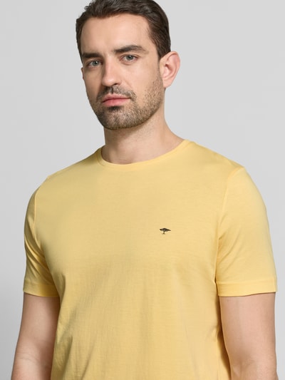 Męski model nosi T-Shirt mit Rundhalsausschnitt und Label-Stitching od Fynch-Hatton, czysta bawełna, krój regular fit, okrągły dekolt, label-stitching, długość tyłu w rozmiarze M: 71 cm, jasny żółty kolor, gładka tekstura, zbliżenie na górną część ciała, widok z przodu.