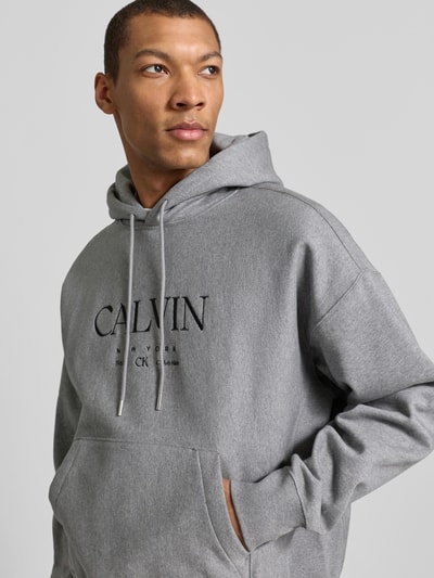 Männermodel trägt Hoodie mit Label-Print und Känguru-Tasche van CK Calvin Klein, mix van katoen en elastaan, relaxed fit, labelprint, kangoeroezak, ruglengte maat M 69 cm, mouwlengte maat M 60 cm, Nahaufnahme Oberkörper