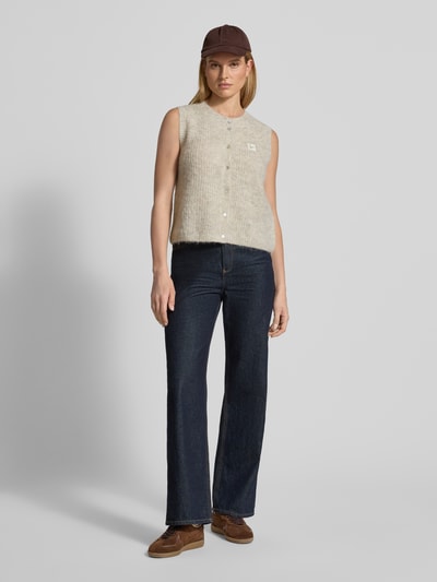 Kobiece modelka nosi Kamizelka w imitacji dzianiny od American Vintage, mieszanka materiałów z domieszką alpaki, krój regular fit, prążkowane wykończenia, okrągły dekolt, listwa guzikowa, detal z logo, długość tyłu w rozmiarze S: 49 cm, widok całej sylwetki z przodu.