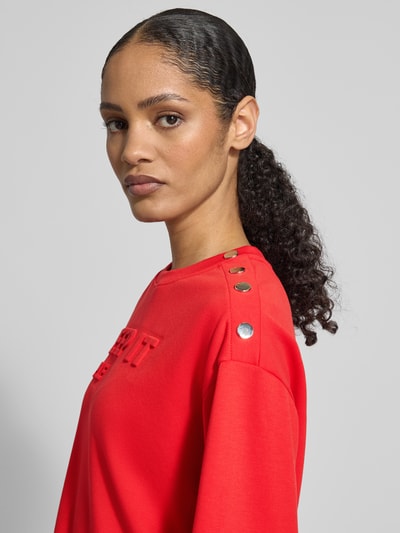 Frauenmodel trägt Sweatshirt mit Viskose-Anteil von monari in Rot mit Nietenbesatz, Statement-Prägung, Nahaufnahme Oberkörper.