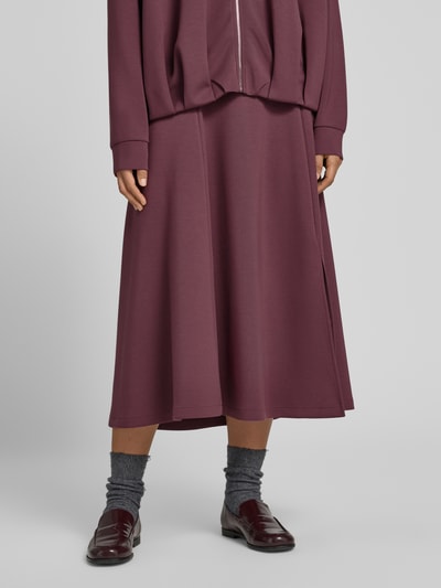 Frauenmodel trägt Midirock mit elastischem Bund von Christian Berg Woman in Bordeaux, glatte Textur, lockerer Schnitt, Nahaufnahme Unterkörper. Elastischer Material-Mix mit Modal-Anteil, Midilänge, Bundweite bei Größe S 80 cm.